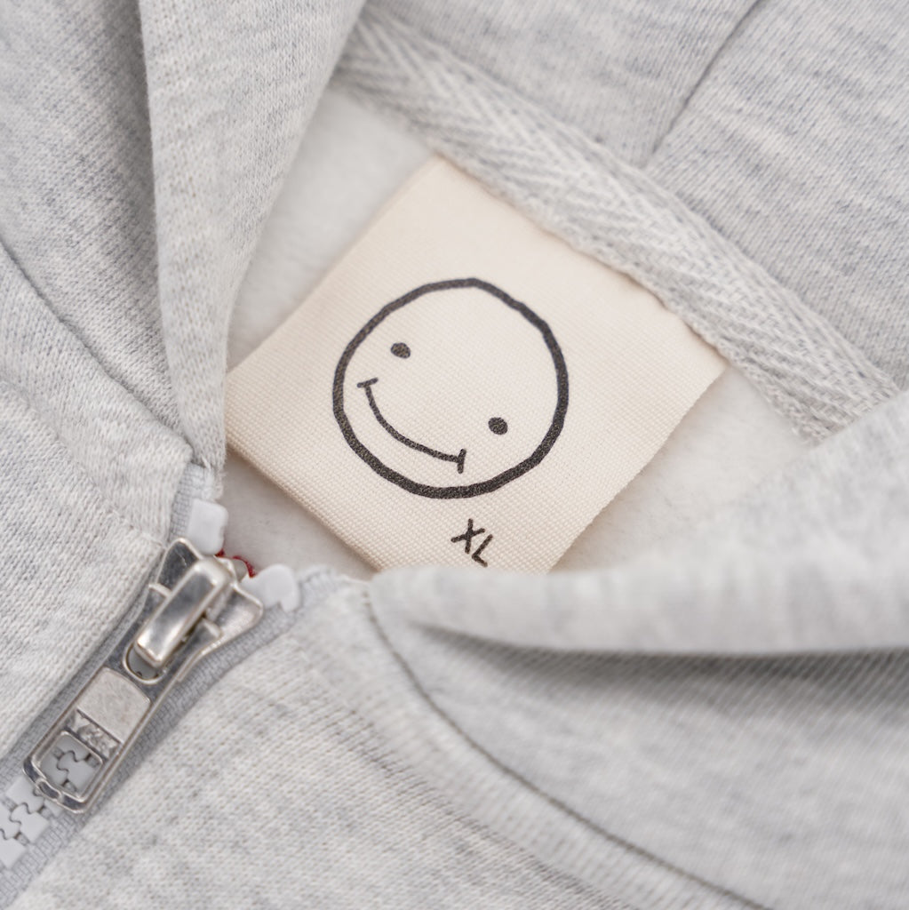 Nahaufnahme des Größenlabels (Größe XL) mit Smiley-Logo im Kragen der grauen LUCREW Patches Hoodie Jacke von LaserLuca